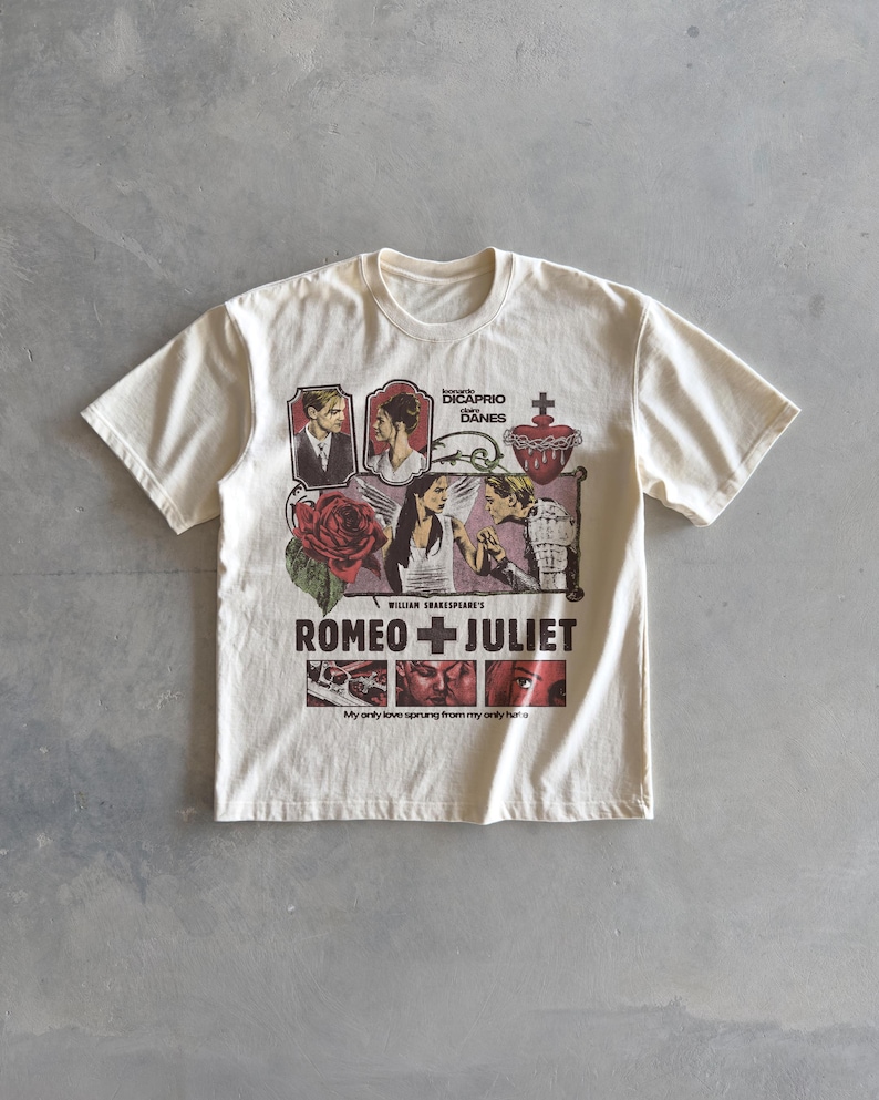 Pu&ograve; includere: Una t-shirt a maniche corte color crema con una stampa grafica del film Romeo + Juliet. Il design include ritratti di Leonardo DiCaprio e Claire Danes, una rosa rossa, un cuore sacro e il testo My only love sprung from my only hate.