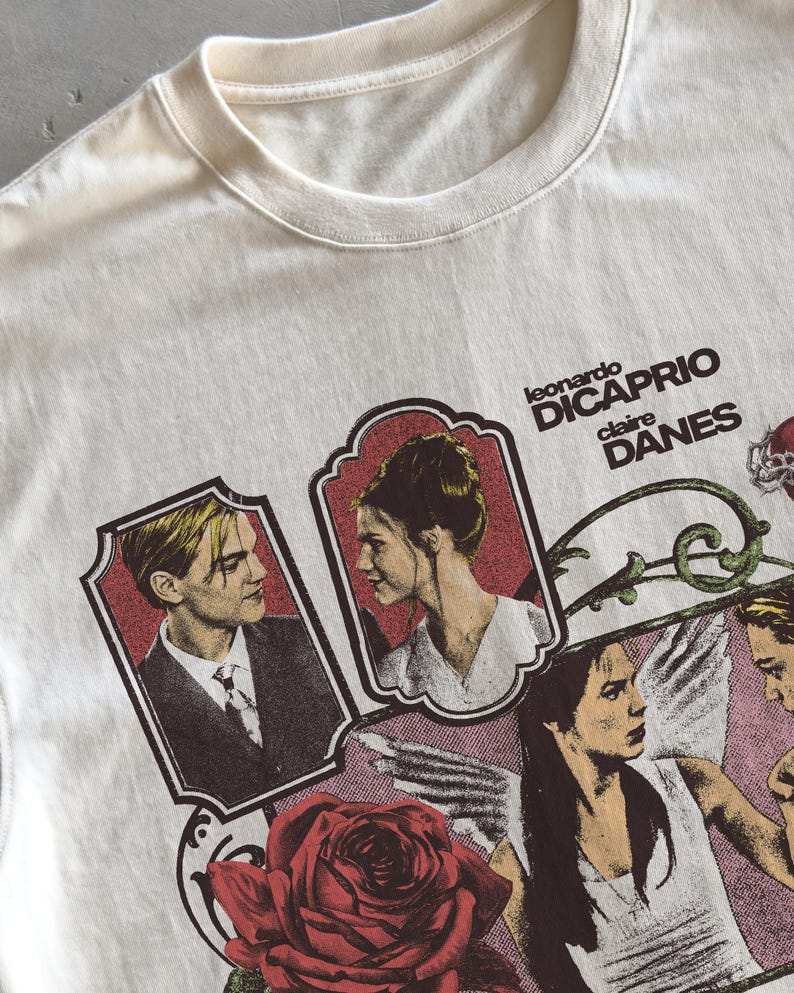 Pu&ograve; includere: Una t-shirt color crema con una stampa grafica di Leonardo DiCaprio e Claire Danes. Il design include due ritratti incorniciati, il testo "leonardo DICAPRIO claire DANES", una grande rosa rossa e l'illustrazione di una figura angelica.