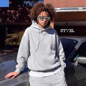 Puede incluir: Conjunto de sudadera con capucha y pantal&oacute;n de ch&aacute;ndal gris claro. La sudadera tiene una capucha con cord&oacute;n y un bolsillo delantero. El pantal&oacute;n de ch&aacute;ndal tiene cintura el&aacute;stica. El texto "5'7"/XL" es visible.