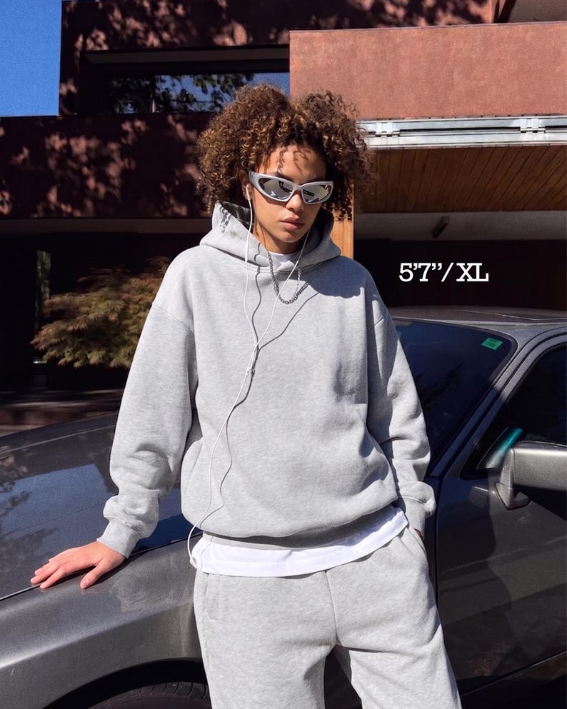 Puede incluir: Conjunto de sudadera con capucha y pantal&oacute;n de ch&aacute;ndal gris claro. La sudadera tiene una capucha con cord&oacute;n y un bolsillo delantero. El pantal&oacute;n de ch&aacute;ndal tiene cintura el&aacute;stica. El texto "5'7"/XL" es visible.