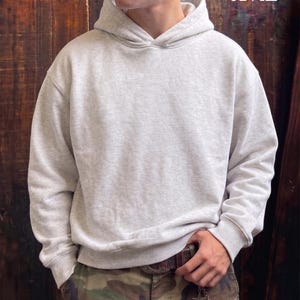 May include: A light gray XL hoodie with a drawstring hood and ribbed cuffs and hem. The hoodie is worn with camouflage pants. The text "6'2"/XL" is visible in the upper right corner.