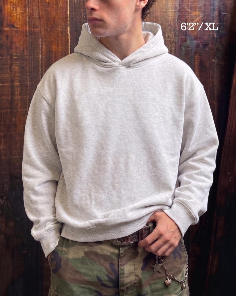 May include: A light gray XL hoodie with a drawstring hood and ribbed cuffs and hem. The hoodie is worn with camouflage pants. The text "6'2"/XL" is visible in the upper right corner.