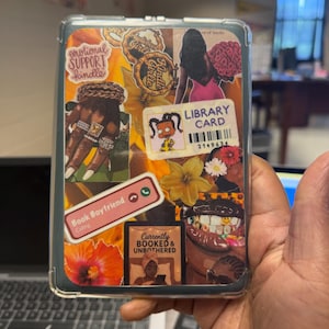 May include: Clear Kindle case with a collage design. The design includes the text "emotional SUPPORT kindle", "LIBRARY CARD", "Book Boyfriend Calling", and "Currently BOOKED & UNBOTHERED". The collage features illustrations of flowers, jewelry, and a woman.