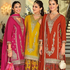 May include: Three outfits consisting of long-sleeved tunics and wide-leg trousers in magenta, mustard yellow, and burnt orange. Each tunic features intricate silver embroidery along the neckline and hem, paired with patterned trousers and matching scarves.