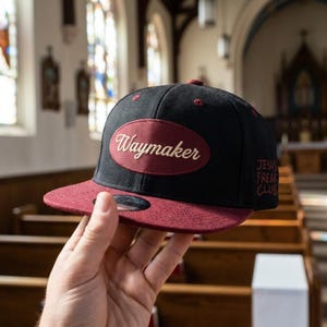 May include: A black baseball cap with a maroon flat brim and a matching maroon oval patch on the front featuring the word Waymaker in cream script. The side of the cap displays the text JESUS FREAK CLUB embroidered in a matching maroon thread.