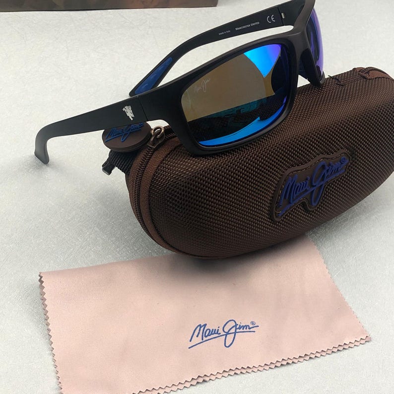 May include: Black sunglasses with blue mirrored lenses rest on a brown case. The sunglasses have a matte black frame and the brand name is visible on the case and cleaning cloth. A light pink cleaning cloth is also included.