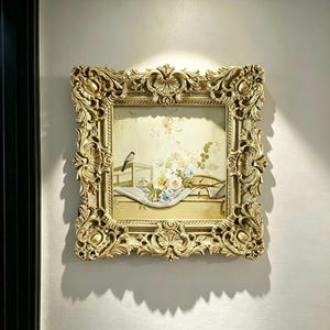 Pode incluir: Uma peça de arte de parede quadrada com uma pintura de um pequeno pássaro pousado numa gaiola ao lado de um ramo de flores brancas, amarelas e azuis, tudo dentro de uma moldura dourada pesada e ornamentada com relevos florais complexos.