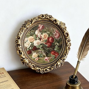 May include: A circular wall art piece featuring a floral painting of red, pink, and white roses encased in an ornate, antique gold-colored frame with intricate scrollwork and floral relief details along the outer edge of the circular border.