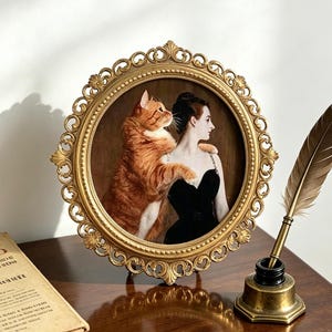 May include: A round, ornate gold-toned picture frame containing a portrait of a person in a black dress with a large orange tabby cat. The frame features intricate scrollwork and floral details along its circular edge.