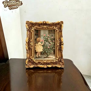 Pode incluir: Uma moldura retangular com um acabamento dourado ornamentado, apresentando padrões intrincados de volutas e relevos florais. A moldura contém uma ilustração de uma criança com um vestido amarelo a cheirar uma roseira com flores cor-de-rosa.