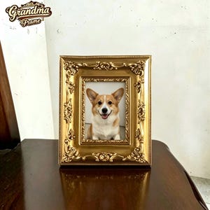 Puede incluir: Un marco de fotos rectangular dorado con detalles ornamentales en relieve, florales y de volutas, a lo largo del borde. El marco contiene una fotografía de un perro Corgi de color canela y blanco. El texto "Grandma Frame" aparece arriba a la izquierda.