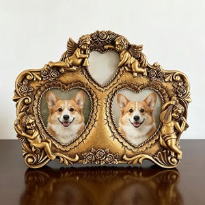 May include: A gold-colored double photo frame with a textured finish, featuring two heart-shaped openings. The frame is decorated with sculpted cherubs and rose motifs. Inside each heart-shaped opening is a photograph of a Corgi dog.