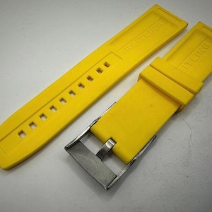 May include: Bright yellow watch strap with a stainless steel buckle. The strap is made of a flexible material and features the brand name "BREITLING" embossed on the surface. The strap has multiple holes for adjustment.