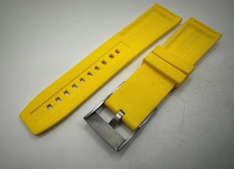May include: Bright yellow watch strap with a stainless steel buckle. The strap is made of a flexible material and features the brand name "BREITLING" embossed on the surface. The strap has multiple holes for adjustment.