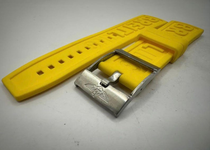 May include: Bright yellow watch strap with the brand name embossed. The strap has a series of square holes for adjustment and is paired with a silver-colored metal buckle. The buckle features a winged emblem.