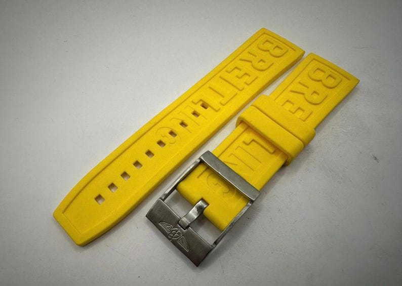 May include: Bright yellow Breitling watch strap with a silver-tone buckle. The strap is made of a flexible material and features the brand name embossed on the band. The buckle has the Breitling logo. This watch accessory is designed for a Breitling watch.