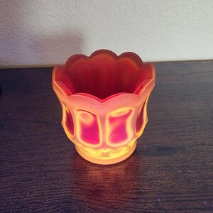 Op de afbeelding: Een decoratieve, tulpvormige kandelaar in tinten rood en oranje. De glazen houder heeft een geschulpte rand en een afgeronde basis. De binnenkant is dieprood, terwijl de buitenkant vervaagt naar een lichter oranje. De kandelaar is ontworpen om een kleine kaars te bevatten.