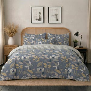 May include: A bedding set featuring a blue duvet cover and matching pillow shams decorated with a pattern of white flowers and tan leaves. The set includes a striped top fold, displayed on a bed with a light brown woven headboard and two framed prints.