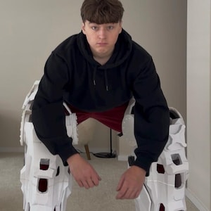 May include: A pair of white robotic leg extensions featuring a complex geometric frame, mechanical joints, and black base platforms. The structure includes visible red accents within the leg segments and small shock absorbers near the feet.