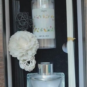 May include: Aromatherapy diffuser set in a black box. Includes a clear glass bottle with a silver cap, a clear glass diffuser bottle, black and white reeds, decorative balls, and a white flower. The set is designed for home fragrance.