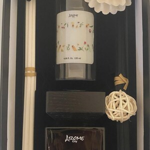 May include: Aromatherapy set in a black box. Includes a clear bottle with floral design, a black diffuser, a white flower, black sticks, and a woven ball. The bottle reads "Arome City" and "4.06 fl. oz. 120 ml."