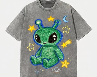 Könnte beinhalten: Ein anthrazitfarbenes T-Shirt in Acid-Wash-Optik mit einer zentralen Grafik eines grünen Alien-Charakters im Buntstift-Stil. Das Design zeigt gelbe Sterne, einen blauen Halbmond, eine Sternschnuppe und ein kleines graues fliegendes Untertassen-Motiv.