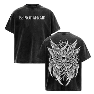 May include: A black acid-wash t-shirt featuring the text BE NOT AFRAID in white on the front. The back displays a detailed white graphic of a multi-eyed, winged creature surrounded by thorny vines, rendered in a high-contrast illustrative style.