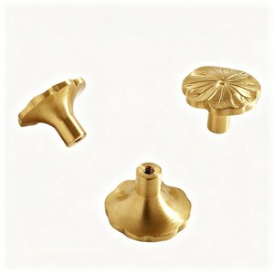 K&ouml;nnte beinhalten: Drei Messing-Schrankkn&ouml;pfe mit floralem Design. Die Kn&ouml;pfe sind in verschiedenen Ausrichtungen, die Vorder-, Seiten- und R&uuml;ckansicht zeigen. Die Kn&ouml;pfe haben eine goldene Oberfl&auml;che vor einem wei&szlig;en Hintergrund.