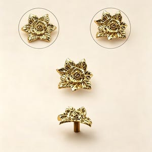 May include: Gold-colored floral cabinet knobs. The knobs are shaped like a rose with detailed petals and leaves. The image shows the knobs from multiple angles, including a close-up and a side view, highlighting the intricate design.