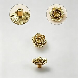 May include: Gold-colored, flower-shaped cabinet knobs. The knobs have a detailed floral design with a stem and mounting hardware. The image includes close-up views of the knob's details, showcasing the intricate petal arrangement and the stem.