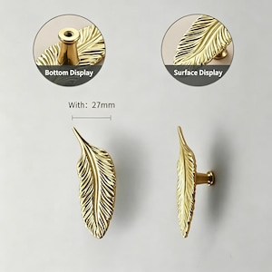 May include: Gold-colored feather-shaped cabinet pulls. The pulls are 27mm wide and feature detailed feather vein patterns. The image includes close-up views of the bottom and surface displays of the hardware.