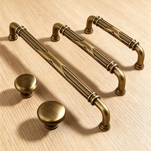 May include: An assortment of antique brass cabinet hardware, including three pull handles and two round knobs. The handles feature a decorative center design and curved ends. The knobs are simple and round. All pieces have a warm, aged finish.