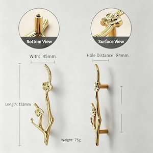 May include: Gold-colored decorative door handles with a floral branch design. The handles are 152mm long, 45mm wide, and weigh 75g. The hole distance is 84mm. The image includes bottom and surface views of the handle.