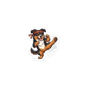 May include: A sticker featuring a cartoon dog with black, brown, and white fur wearing an orange headband. The dog is captured in a dynamic martial arts pose, performing a high side kick with one leg extended while its mouth is open in a smile.