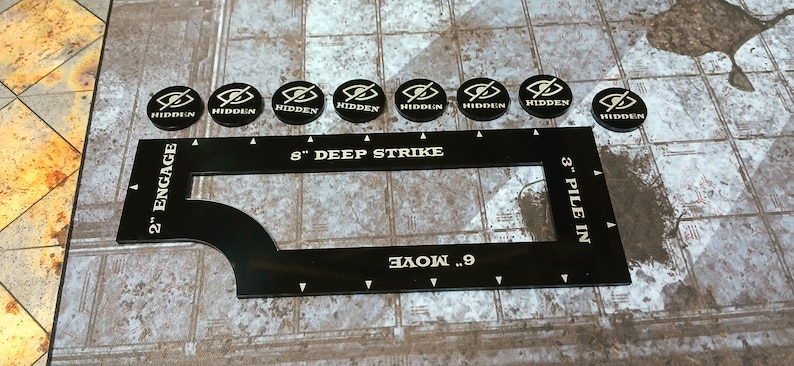 May include: Black gaming accessories. Eight round tokens feature a stylized eye logo and the word "HIDDEN". A black ruler-shaped game piece reads "8" DEEP STRIKE", "6" MOVE", "2" ENGAGE", and "3" PILE IN".