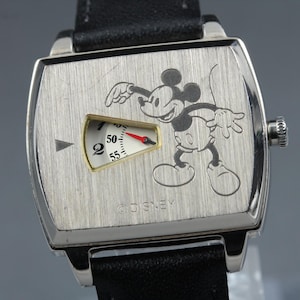 May include: A rectangular silver-tone wristwatch with a black leather strap. The brushed metal face features an engraved Mickey Mouse illustration, a gold-rimmed triangular window displaying a partial dial with numbers 2, 50, 55, and a red hand.