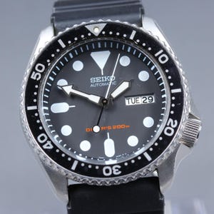 May include: A Seiko automatic wristwatch with a black dial and a black rotating bezel. The watch features white hour markers, luminous hands, and a date display. The watch has a black rubber strap and a stainless steel case. The dial reads "SEIKO AUTOMATIC" and "DIVER'S 200m".
