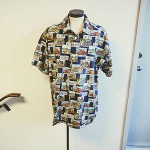 Könnte beinhalten: Kurzärmeliges Hemd mit Knopfleiste und einem sich wiederholenden Muster aus Oldtimern und Nummernschildern auf marineblauem Hintergrund. Das Hemd wird auf einer Schaufensterpuppe präsentiert, um seinen lässigen Stil und sein lebendiges Design hervorzuheben.