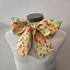 May include: A green bow tie with a mushroom pattern. The mushrooms are red, pink, blue, and yellow.