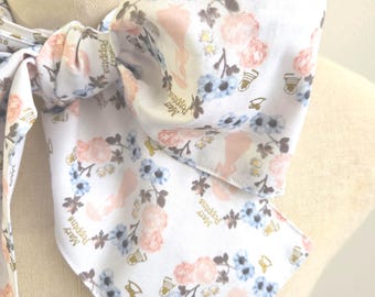 May include: A white fabric neck scarf featuring a repeating pattern of light blue and pink flowers, small gold-colored umbrellas, and silhouettes of a figure holding an umbrella, with the text Mary Poppins printed in gold lettering.