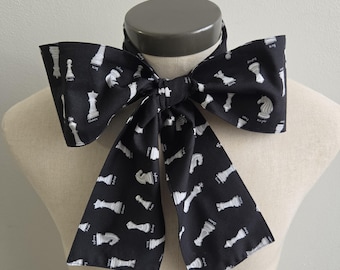 May include: A black necktie featuring a repeating white print of various chess pieces including kings, queens, bishops, knights, rooks, and pawns. Each chess piece is labeled with its corresponding name in white text printed directly onto the fabric.