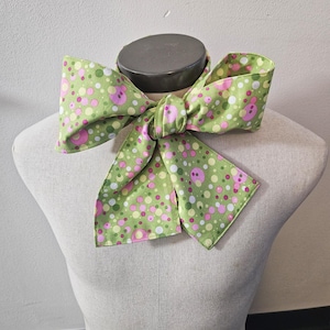 May include: A green fabric bow tie with a white background and pink and green polka dots.