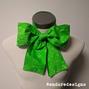 May include: A green bow tie with a white speckled pattern. The bow tie is tied around a mannequin's neck. The text "@enduredesigns" is visible at the bottom of the image.