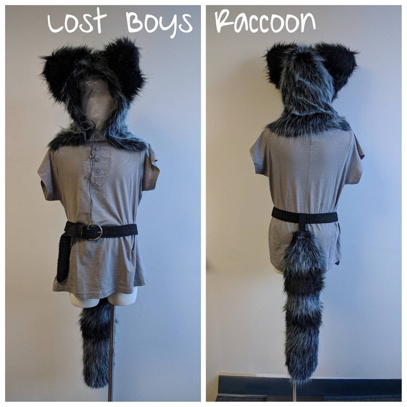 May include: A gray shirt with a black belt and a raccoon tail attached. The shirt has a black fur hood with ears. The text "Lost Boys Raccoon" is written at the top of the image.