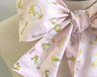May include: A light pink fabric bow featuring a repeating gold glitter print of the Mary Poppins silhouette holding an umbrella inside a white dotted circle, with the text Mary Poppins printed in gold script throughout the fabric pattern.