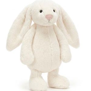 May include: A plush, cream-colored bunny with long, floppy ears and a pink nose. The stuffed animal has a soft, textured appearance and is standing upright. The bunny's eyes are black, and its paws are rounded. A children's toy.