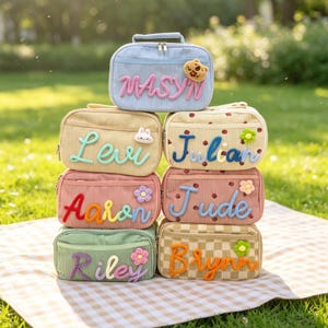 May include: A stack of colorful corduroy bags, each with a name embroidered in a contrasting color. The bags are in shades of blue, yellow, pink, and green, with decorative accents like flowers and a bear.