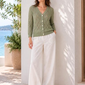 May include: A sage green V-neck cardigan featuring a diamond-patterned knit texture, long sleeves, and a front button closure, paired with wide-leg white trousers. The cardigan has ribbed cuffs and a ribbed hem, while the trousers are full-length.