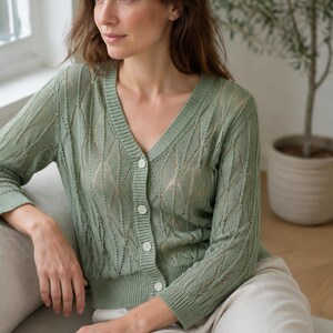 May include: A sage green V-neck cardigan featuring a delicate openwork knit pattern with vertical diamond-shaped motifs. The garment has long sleeves, a ribbed hem and cuffs, and is fastened down the front with four small, round, light-colored buttons.