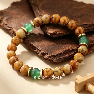 May include: A beaded bracelet featuring round, mottled brown and tan jasper-like stones interspersed with smooth, translucent green beads and small, polished gold-tone metal spacers. The text ROSYLUME is printed in white at the bottom.